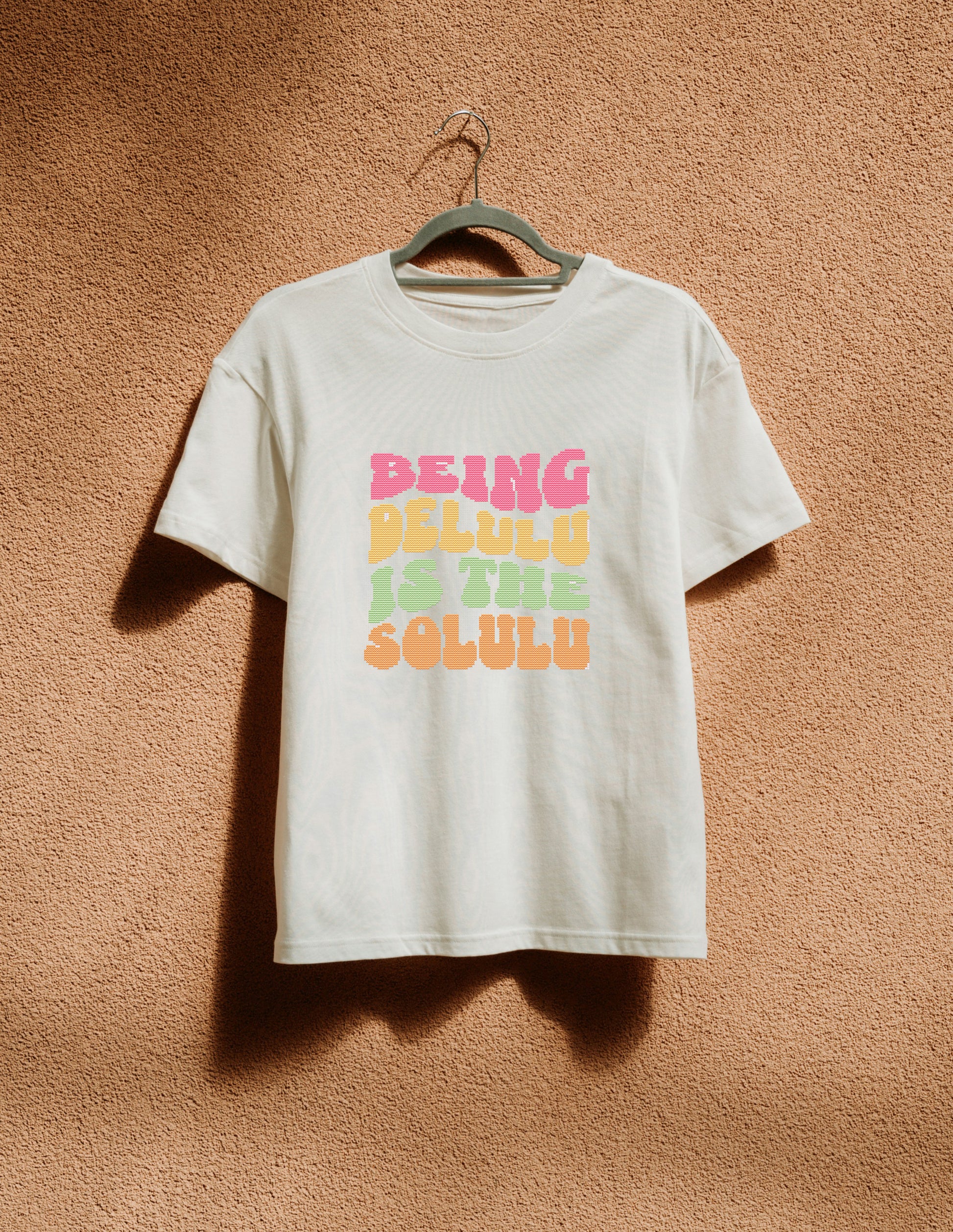 White t-shirt with colorful text on a hanger against a brown textured wall