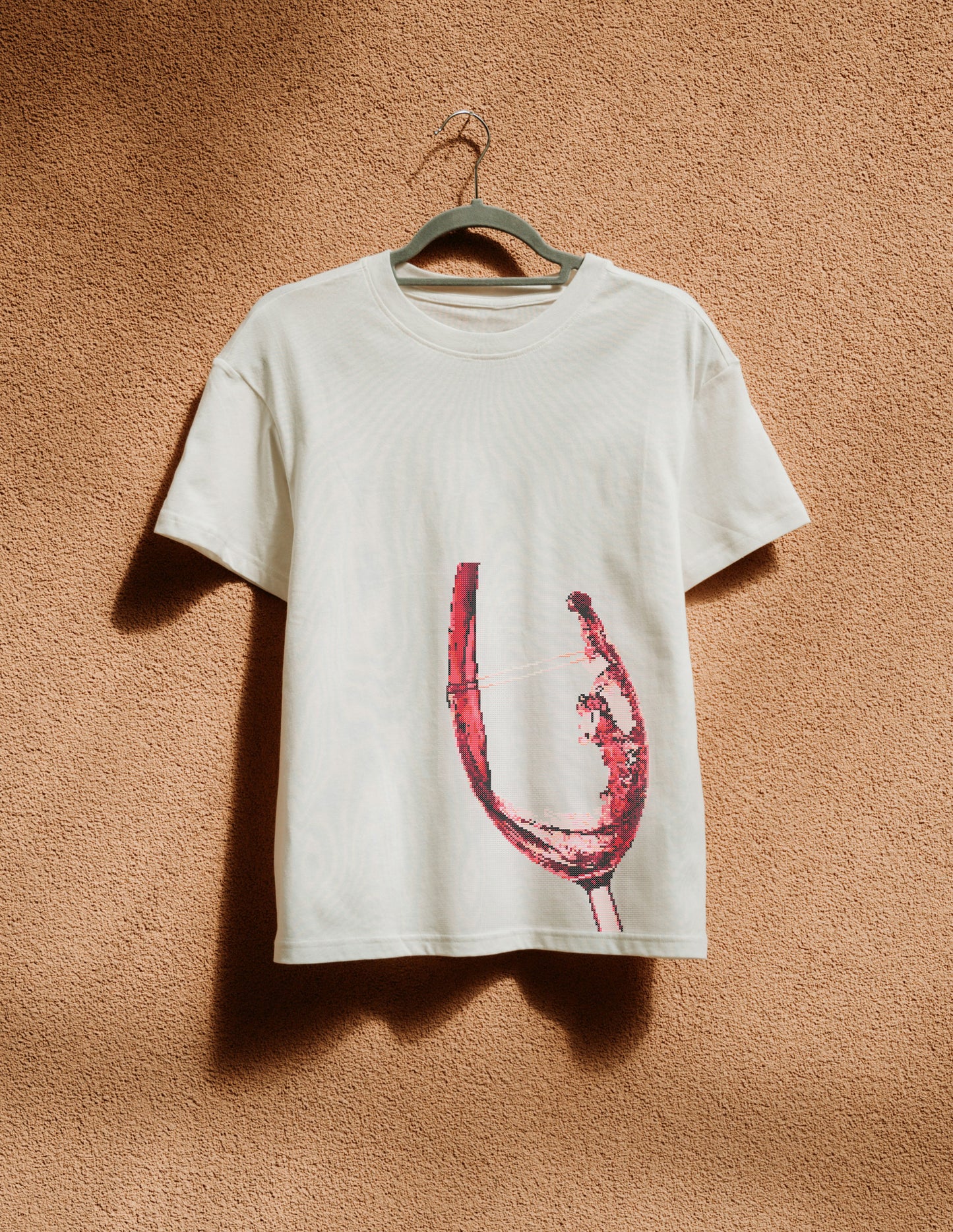 White t-shirt with a red graphic design on a hanger against a beige wall