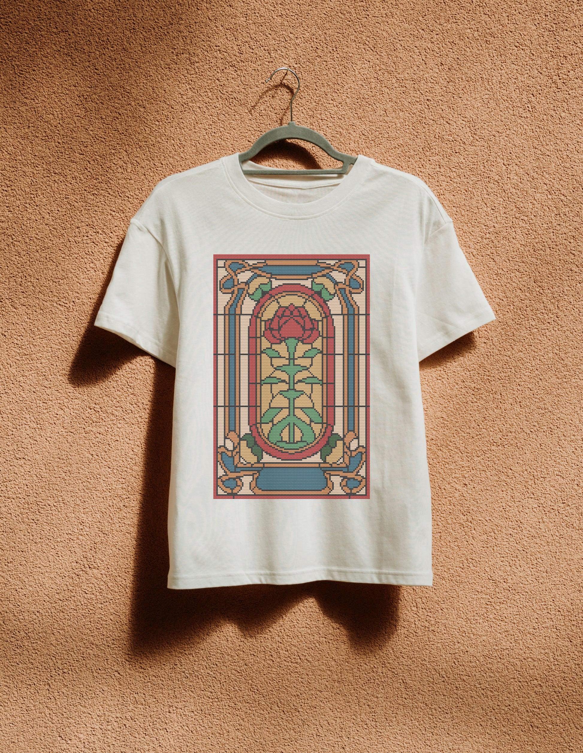 White t-shirt with stained glass design on a hanger against a textured brown wall