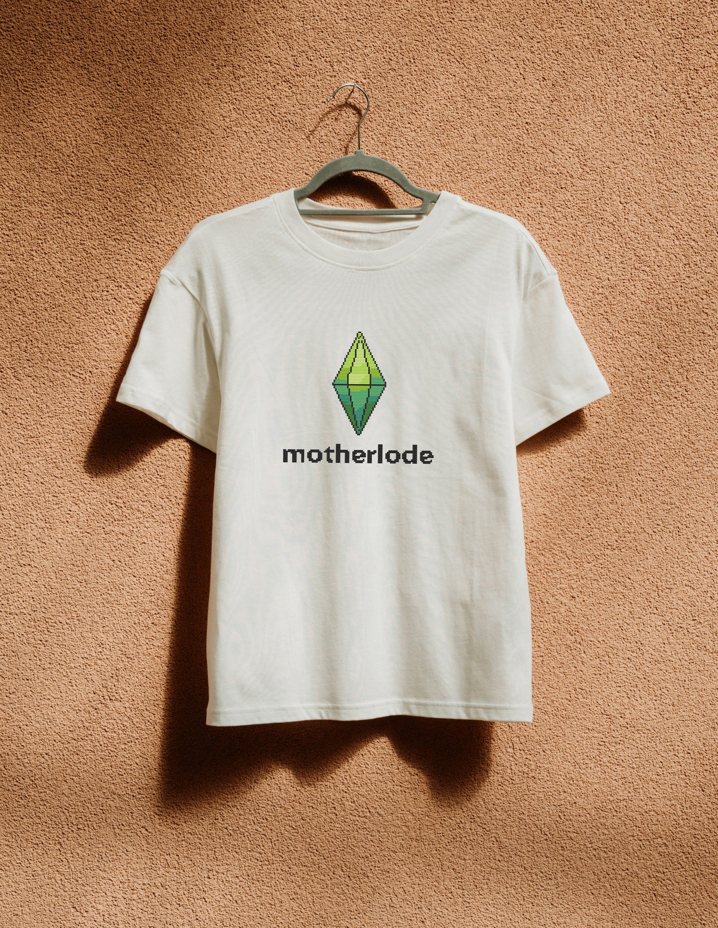 White t-shirt with 'motherlode' and logo on a hanger against a brown textured wall