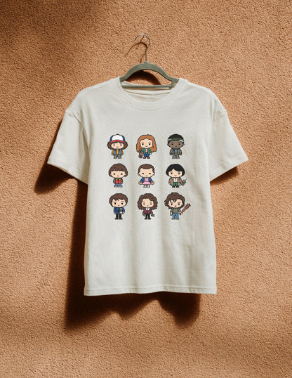 White t-shirt with pixelated character designs on a hanger against a brown textured wall.