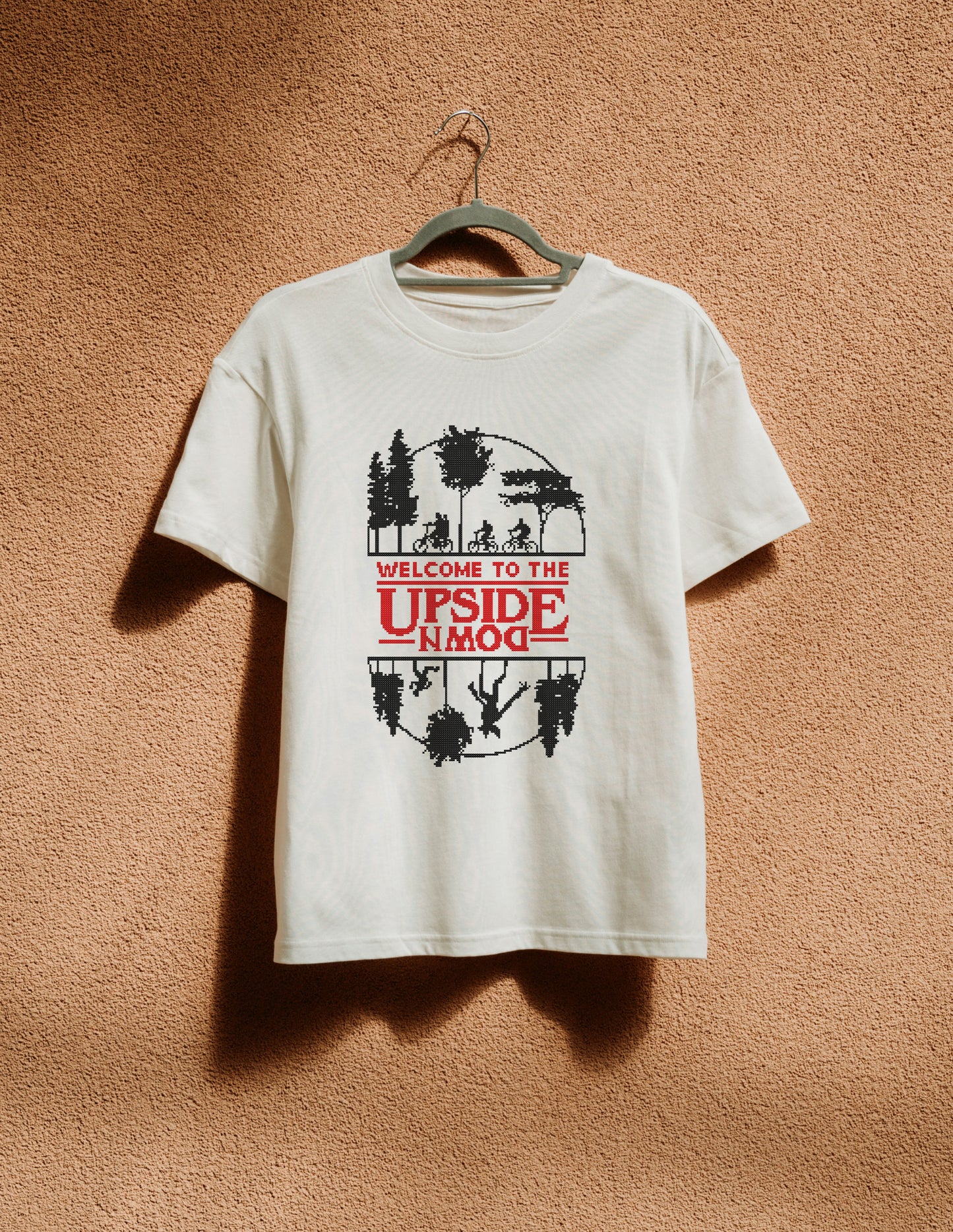 White t-shirt with graphic design on a hanger against a brown textured wall