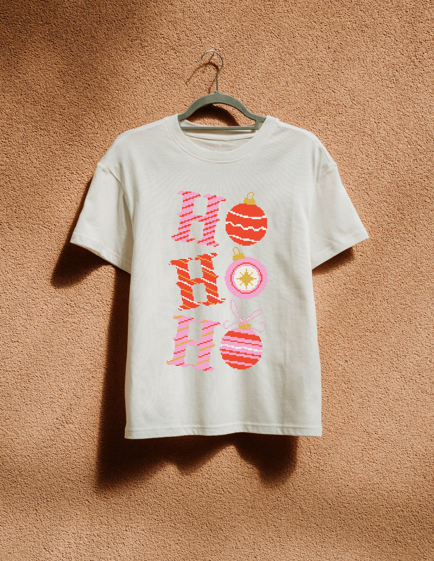 White t-shirt with 'Ho Ho Ho' design on a hanger against a brown textured wall