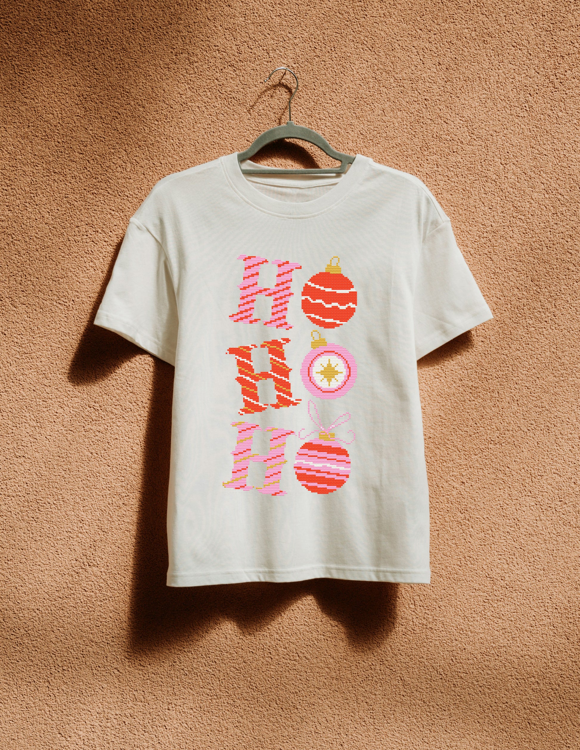 White t-shirt with 'Ho Ho Ho' design on a hanger against a brown textured wall